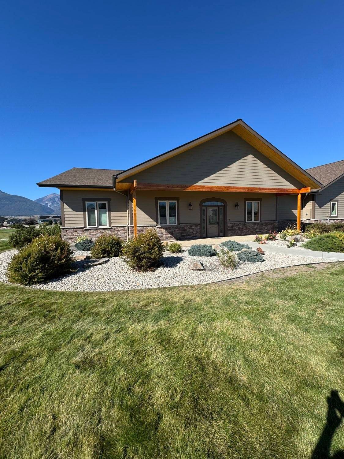 Tan building with brown trim and windows, surrounded by a lawn and decorative rock landscaping, under a blue sky.