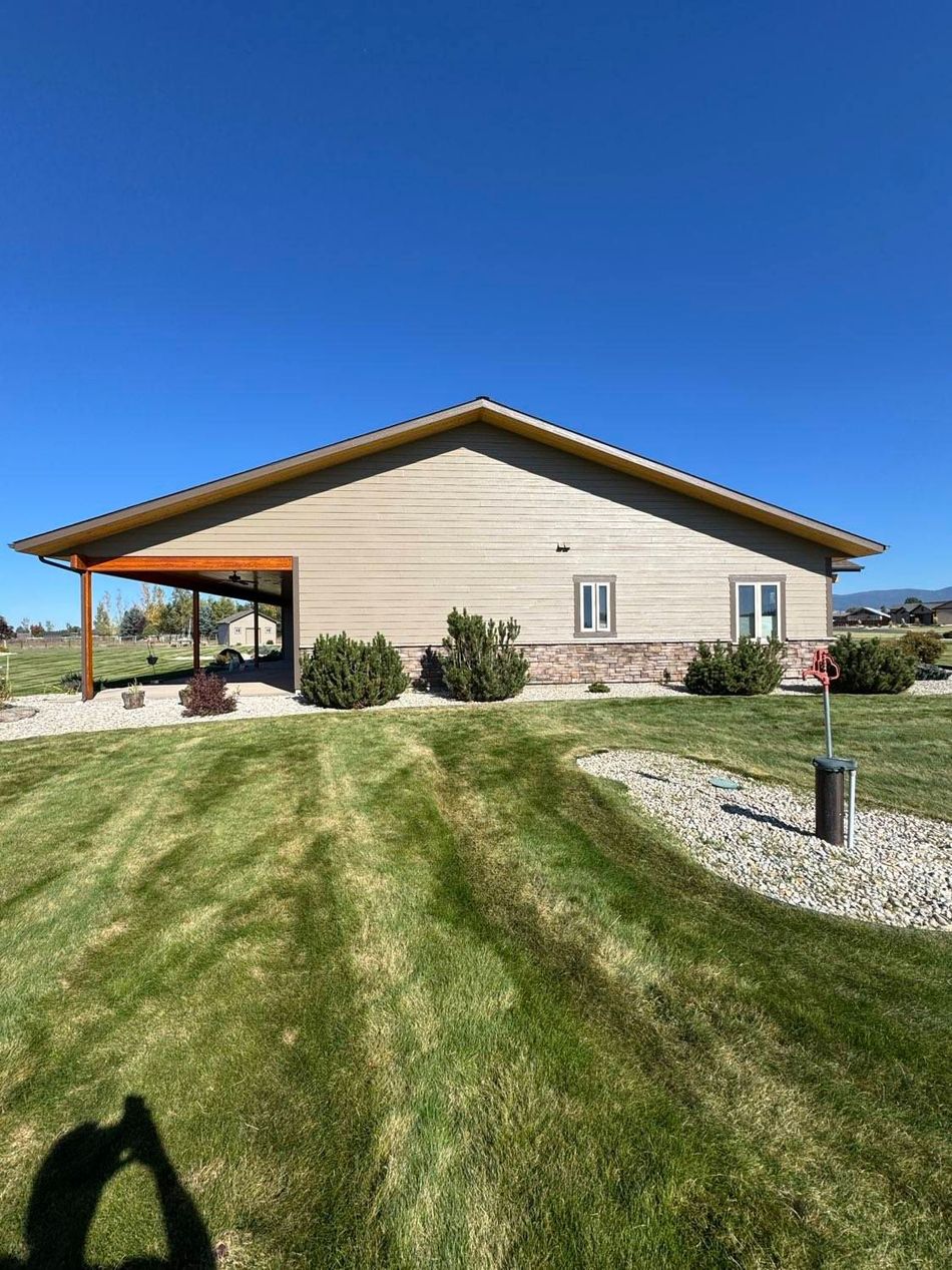 Tan building with covered porch and brown trim, set on green lawn under a blue sky.