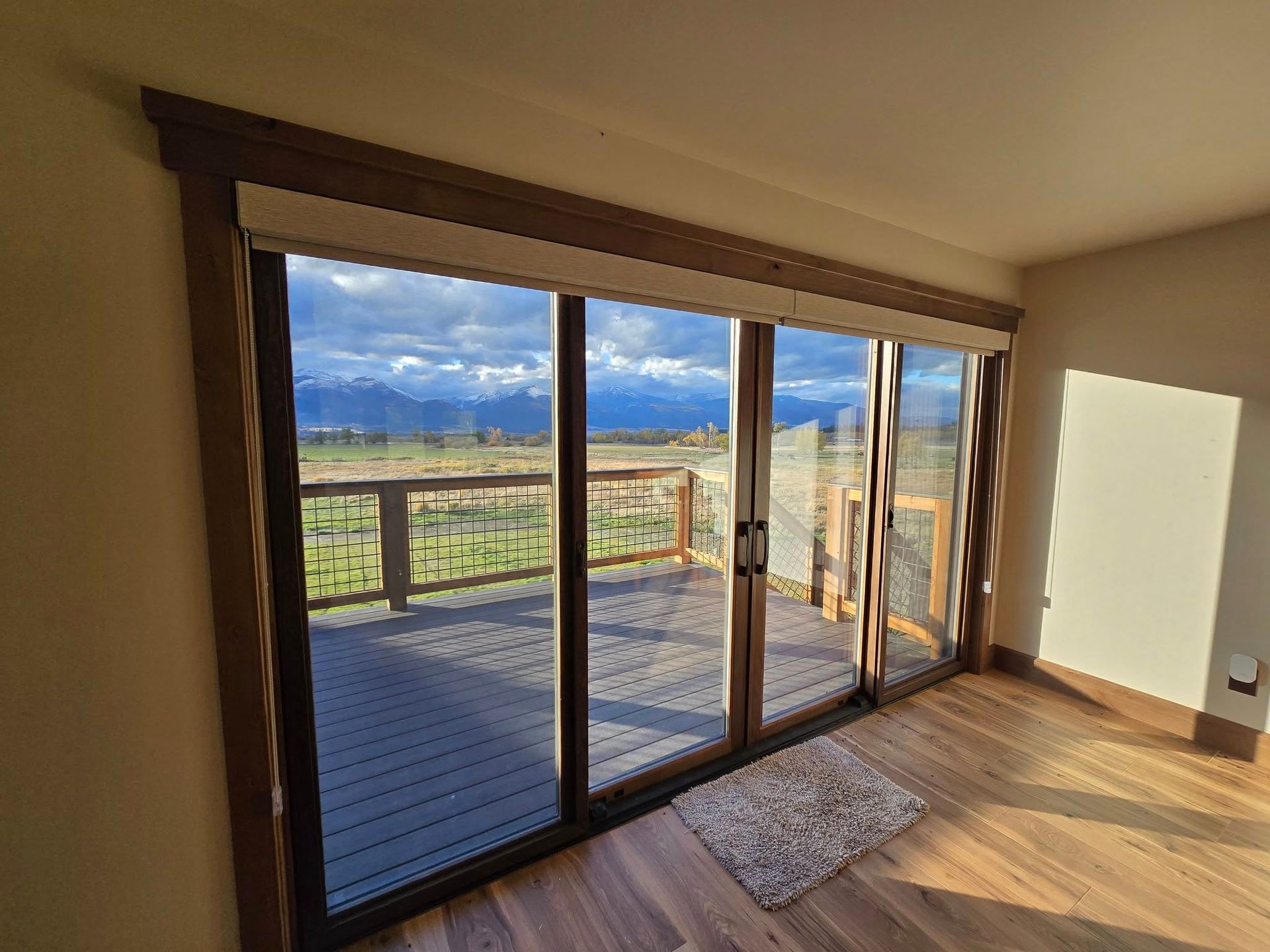 Sliding glass doors offer a view of a wooden deck and mountain range, framed by dark wood.