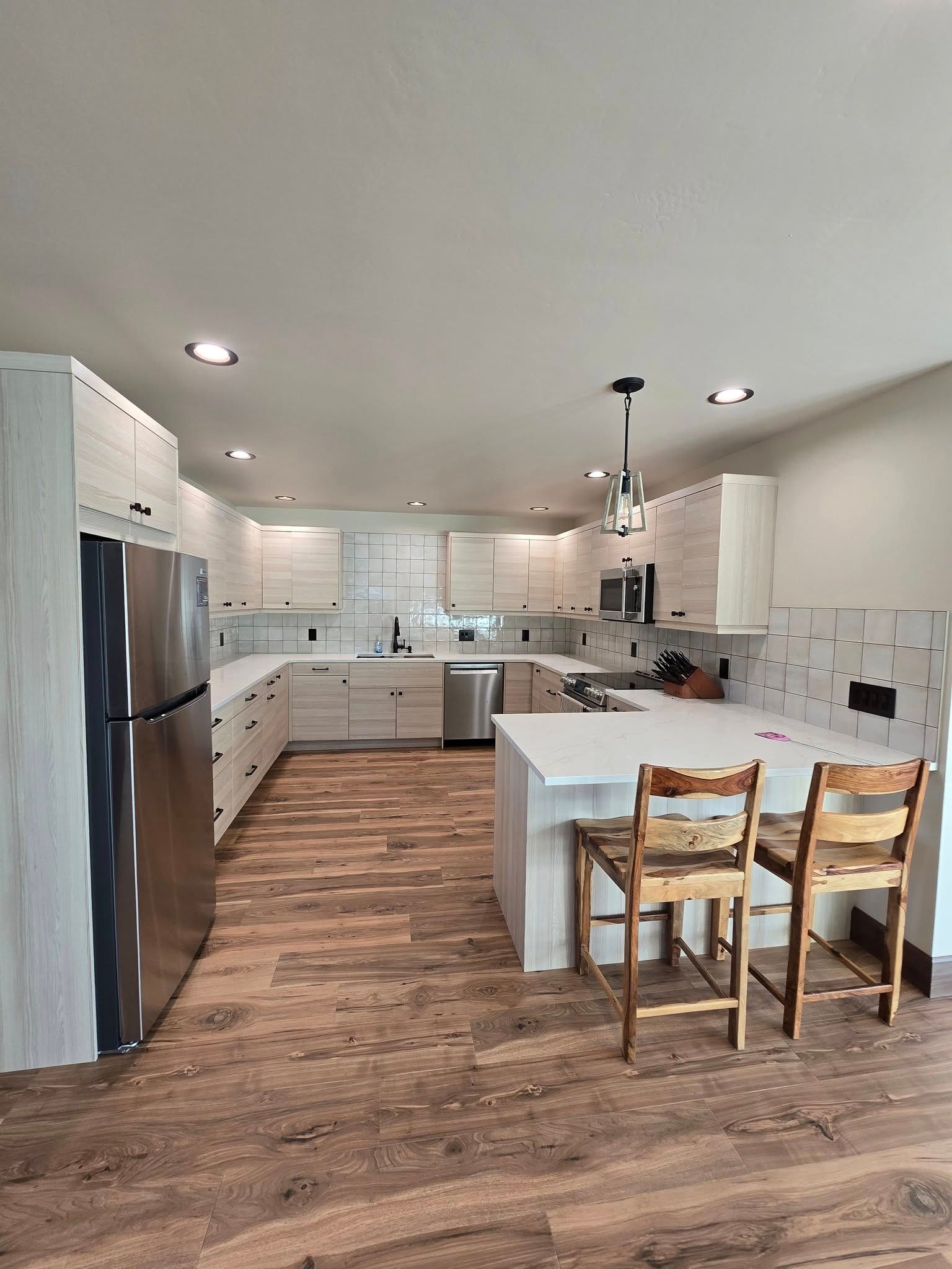 Modern kitchen with light wood floor, white cabinets, stainless steel appliances, and breakfast bar.