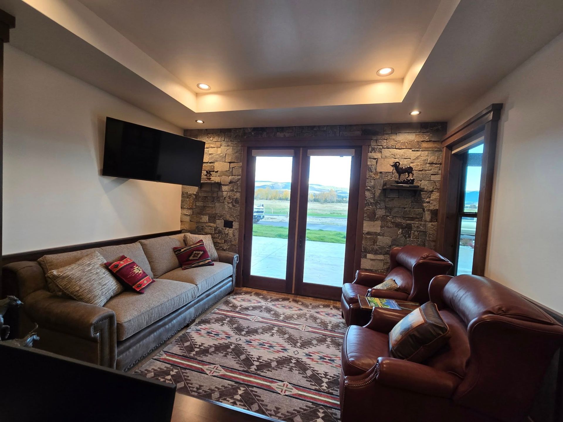 Living room with stone accent wall, TV, brown leather chairs, and a sofa.