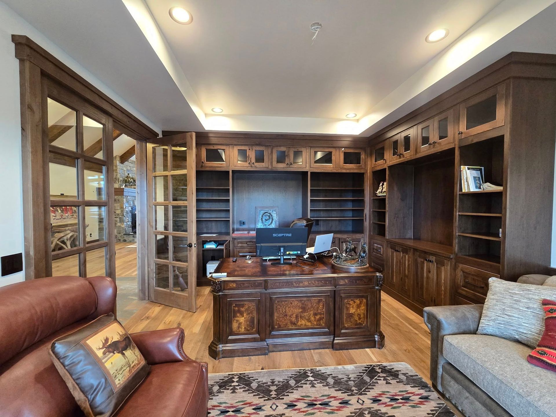 Home office with dark wood built-in shelves, desk, leather chairs, and open French doors to another room.