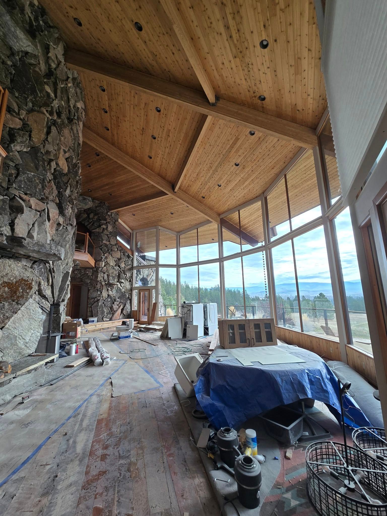 Sunroom under renovation with rock fireplace, glass walls, and wood ceiling.