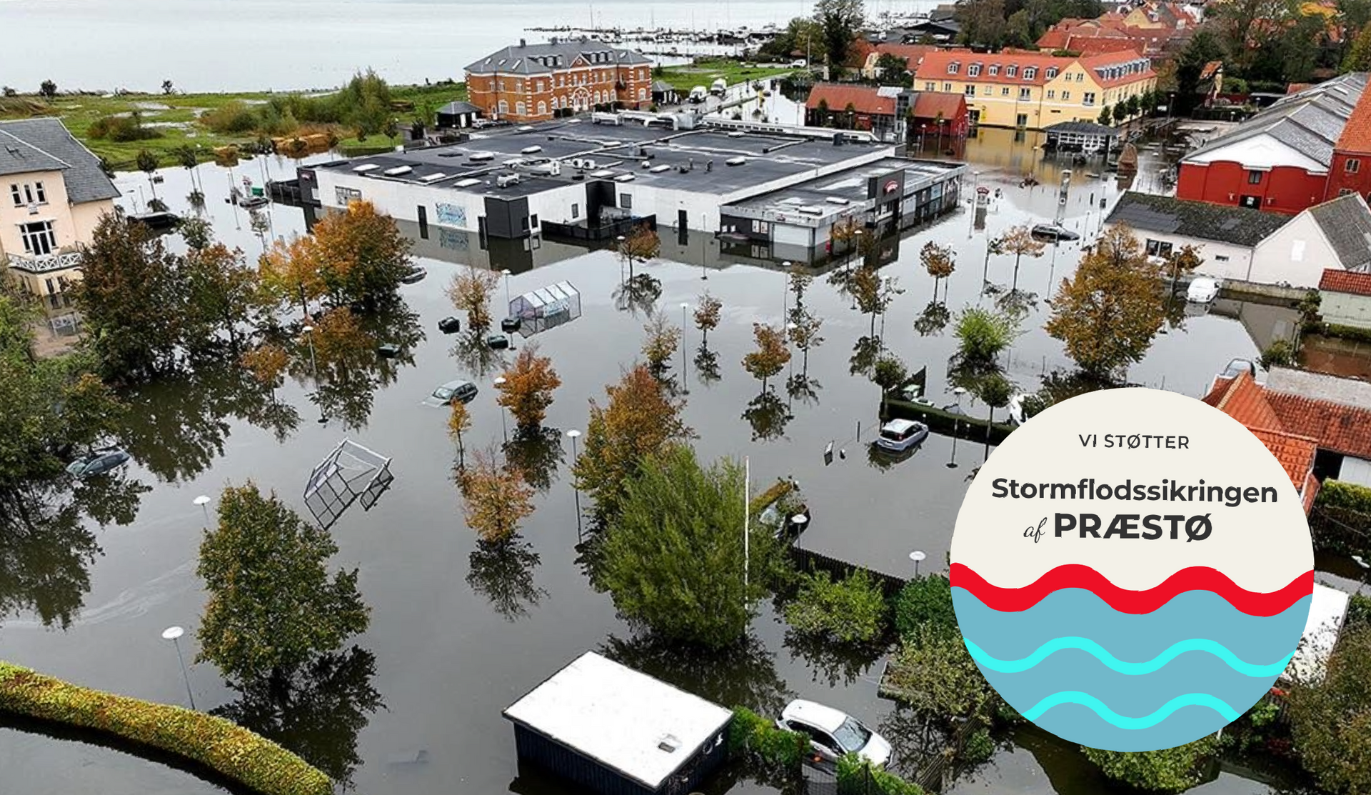 Billede over Præstø under stormfloden i oktober 2023. Logo med: Vi Støtter Stormflodssikringen af Præstø