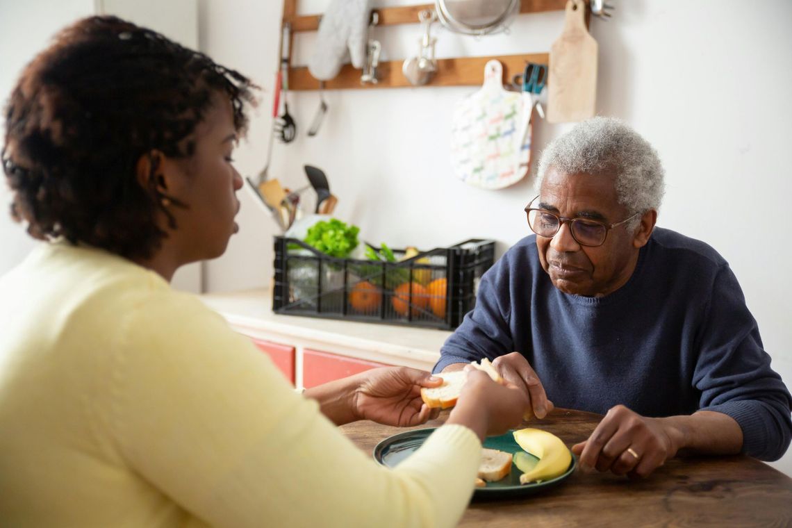 Woman assisting a person at a table, cutting food onto a plate in a kitchen.