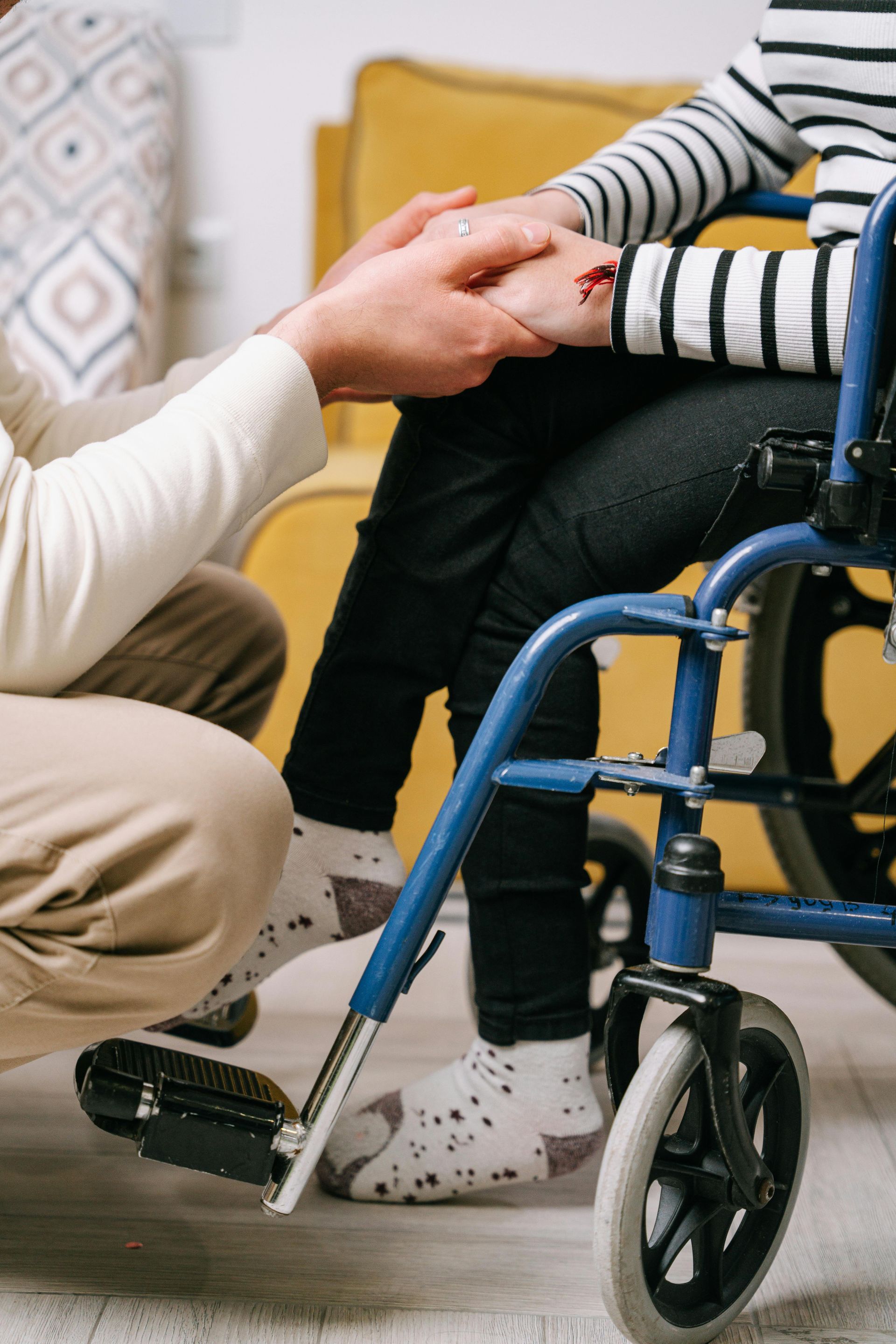 Person holding hands with someone in a wheelchair, offering comfort.