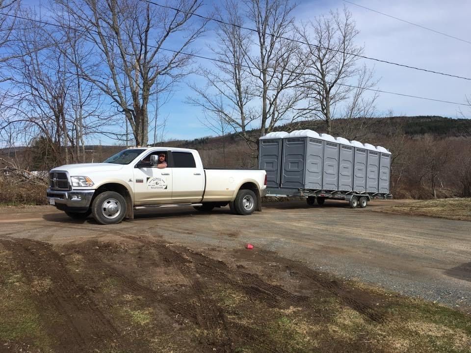 A white truck is towing a trailer with portable toilets on it.