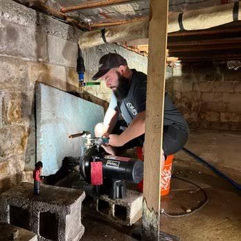 Worker using a power saw in a dim basement beside concrete blocks and pipes