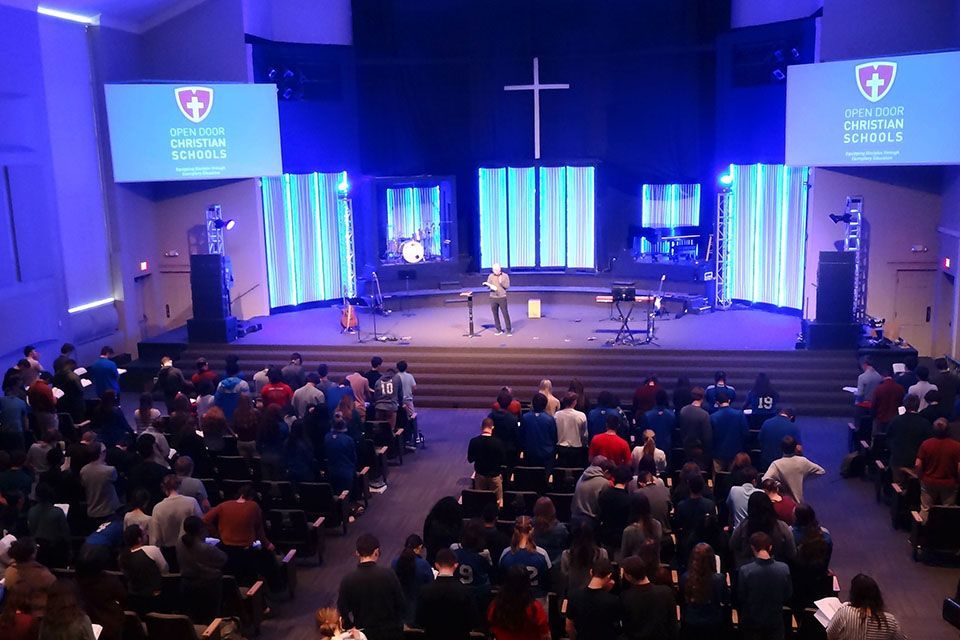 a large group of people are sitting in front of a stage that says open door christian school