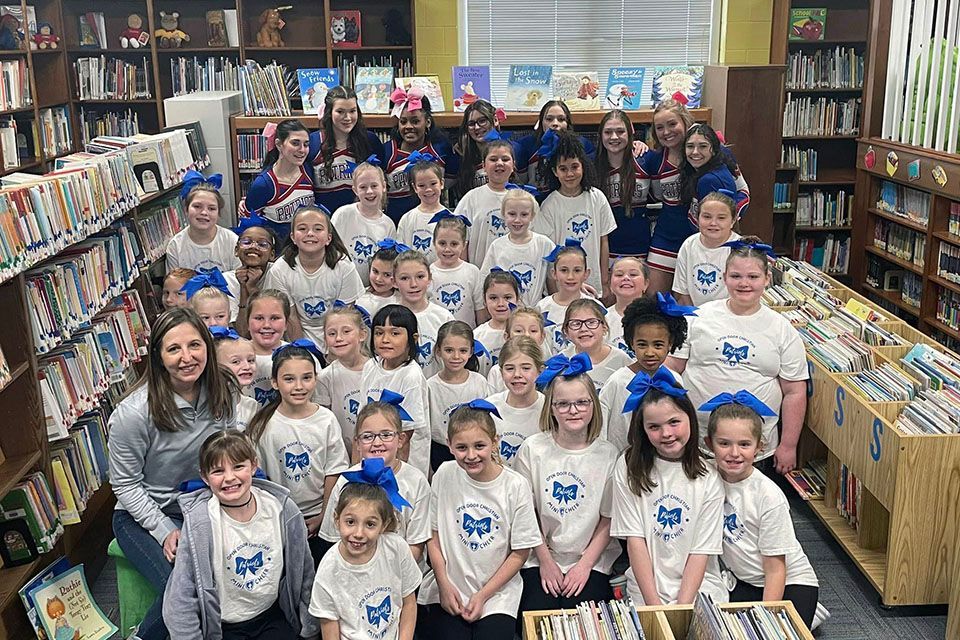 a group of cheerleaders wearing white shirts with blue bows are posing for a photo in a library