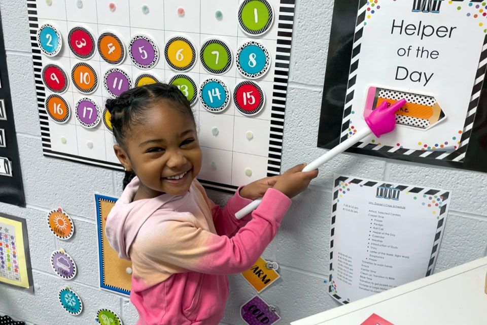 a little girl in front of a helper of the day sign