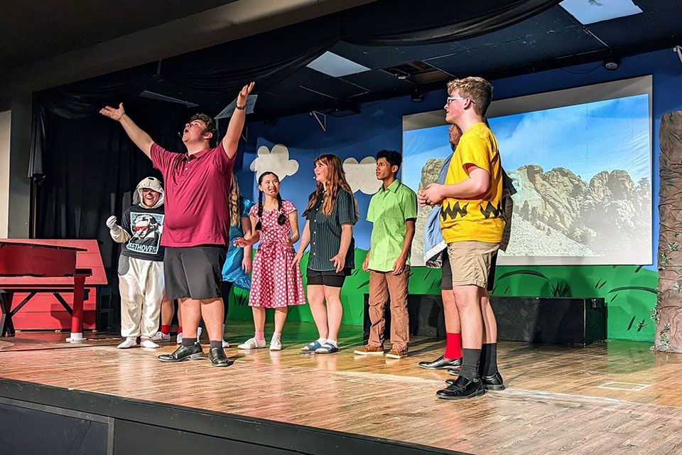 a group of people on a stage with one wearing a yellow shirt that says peanuts