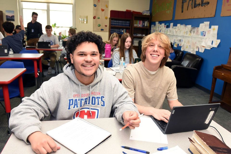 a boy wearing a patriots sweatshirt sits at a desk