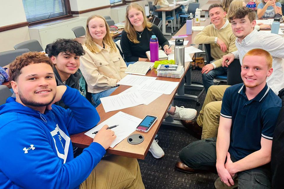 A group of students are sitting around a table in a classroom.