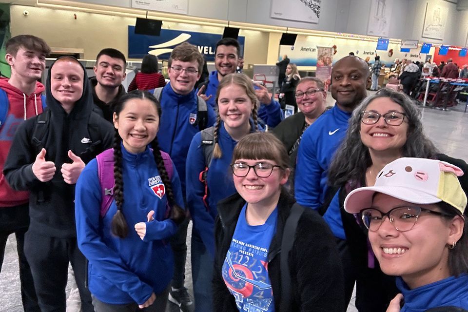 Students and adults are posing for a picture in an airport.