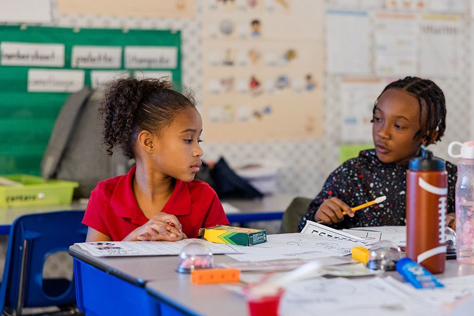 Two young girls are sitting at a table in a classroom.