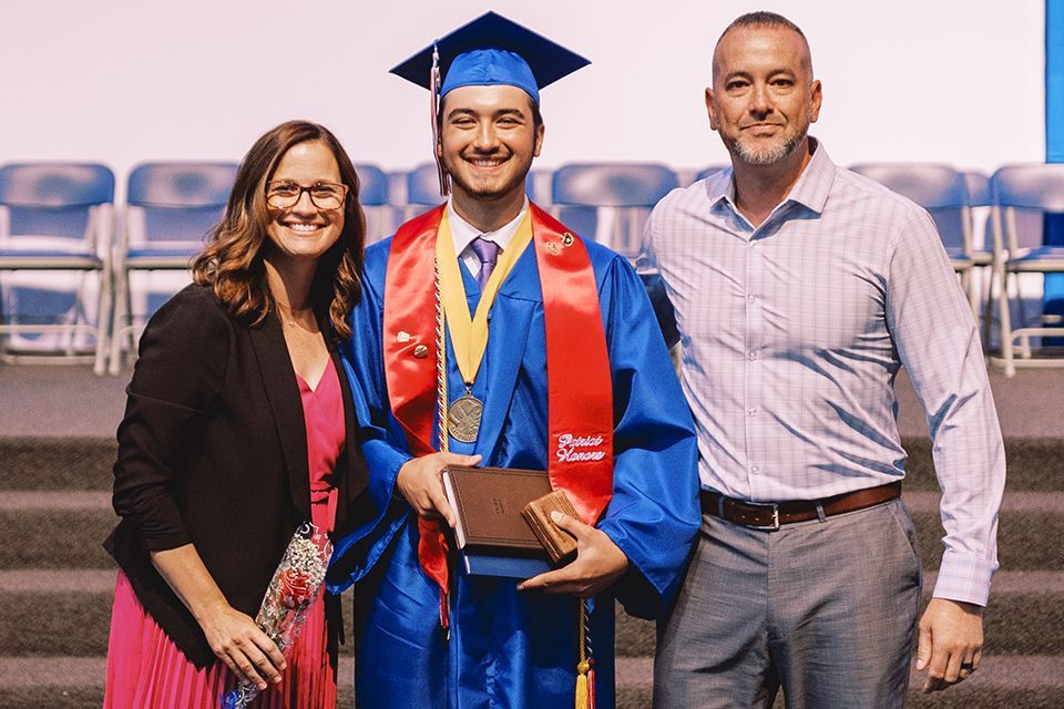 An ODCS graduate poses for a picture with his parents.