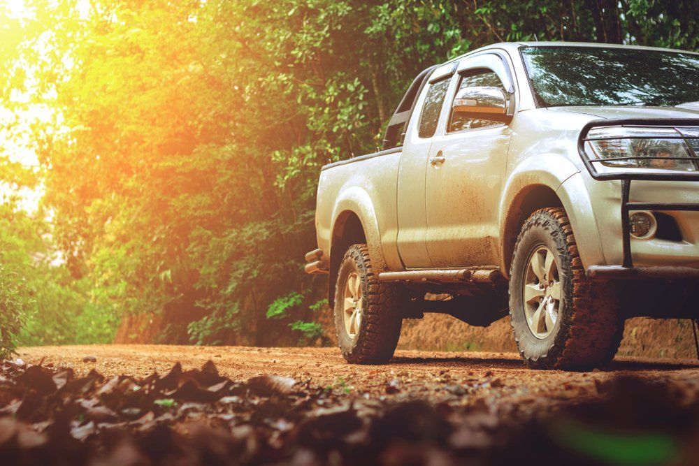 A White Truck Is Parked on A Dirt Road in The Woods — Emu Park Automotive and Tyre Service in Emu Park, QLD