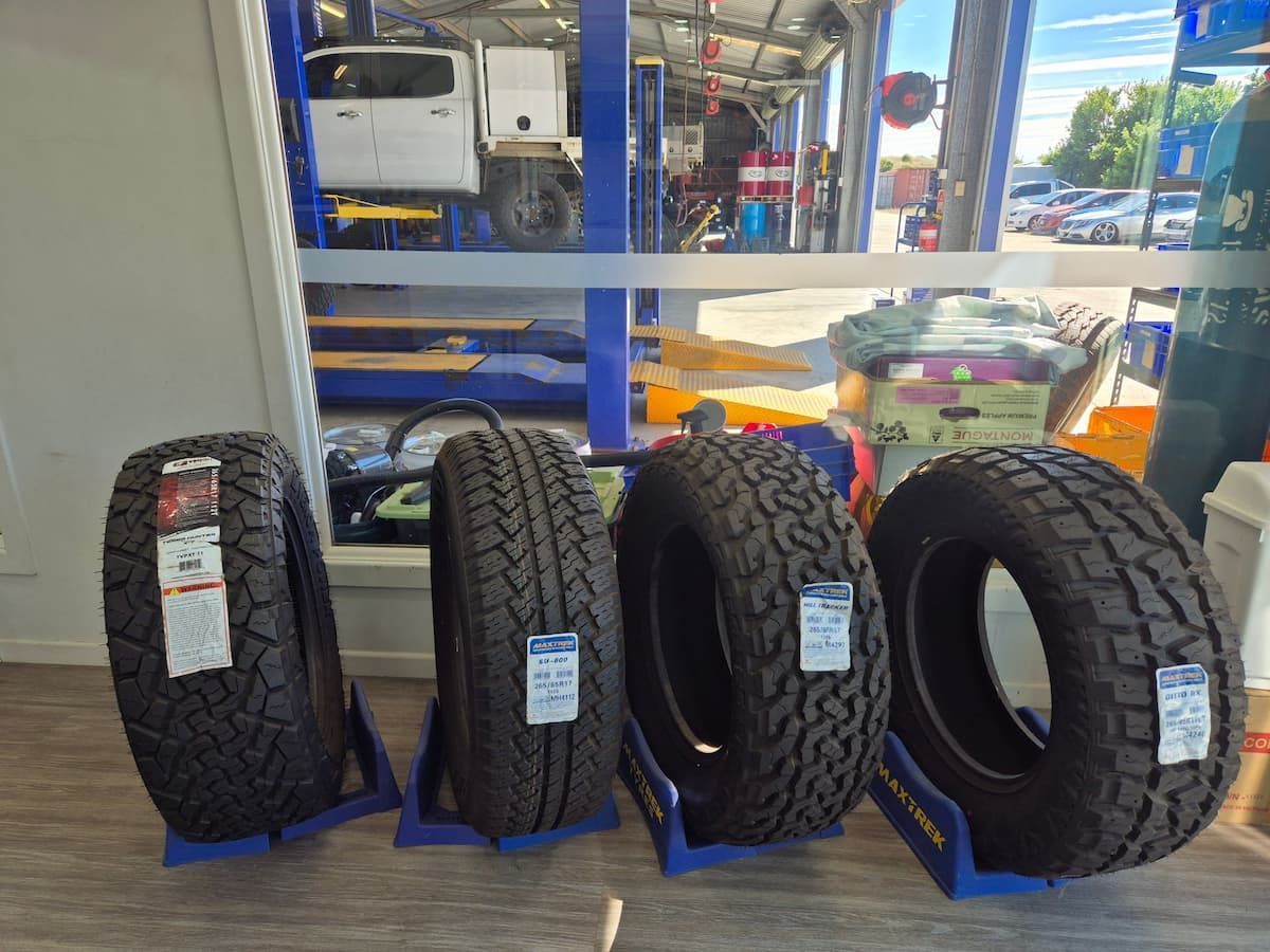 Four black off-road tires displayed on blue stands in a tire shop.  — Emu Park Automotive and Tyre Service in Emu Park, QLD