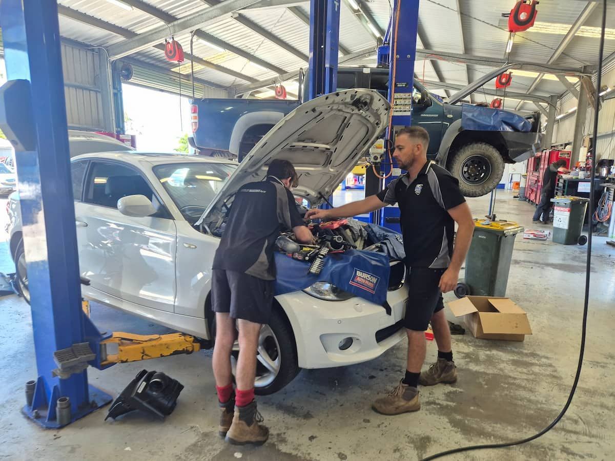 Two mechanics working on a white car in an auto repair shop, hood open on a lift.  — Emu Park Automotive and Tyre Service in Emu Park, QLD