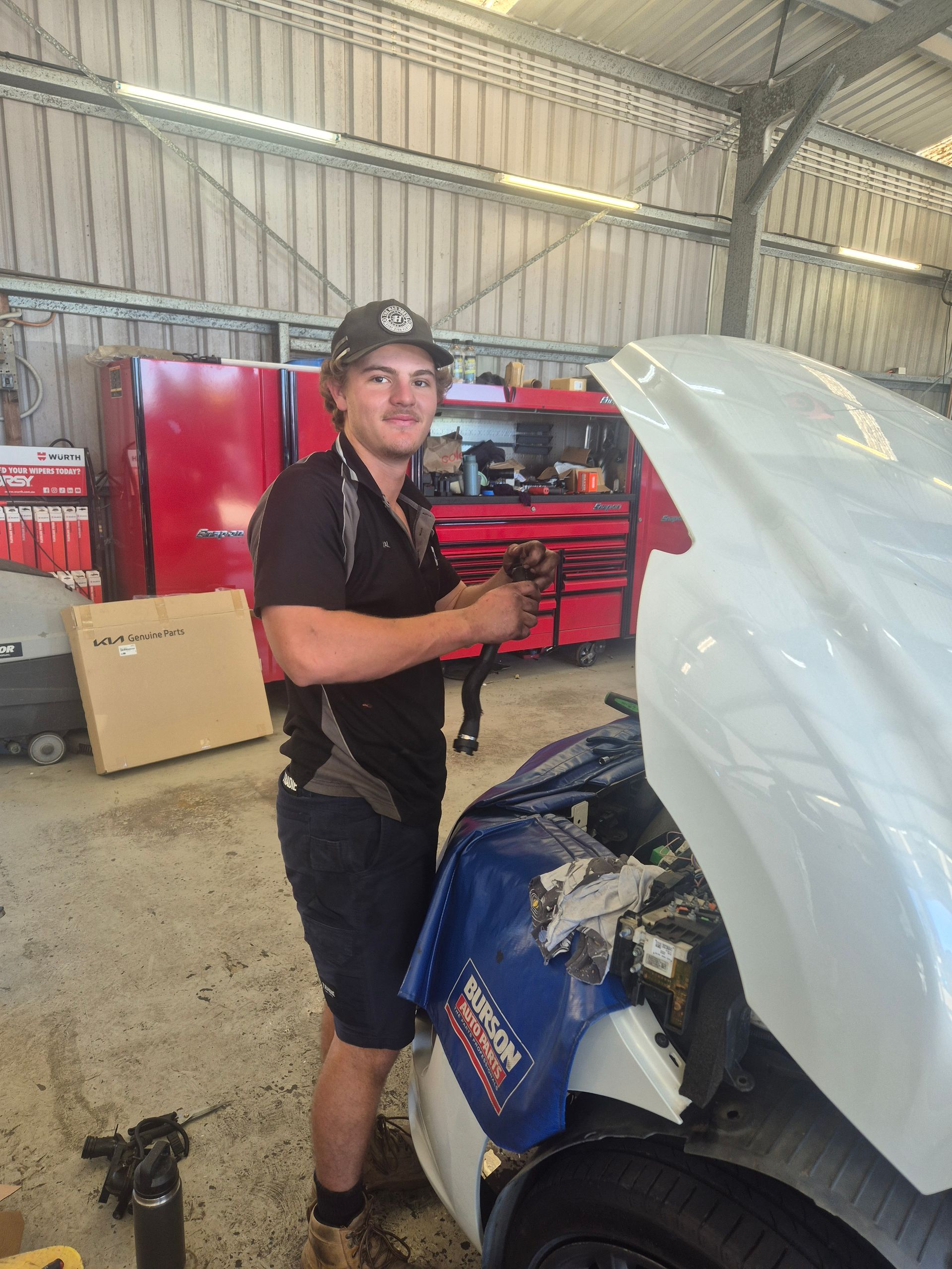 Mechanic working beside a blue car with the hood open inside a garage  — Emu Park Automotive and Tyre Service in Emu Park, QLD