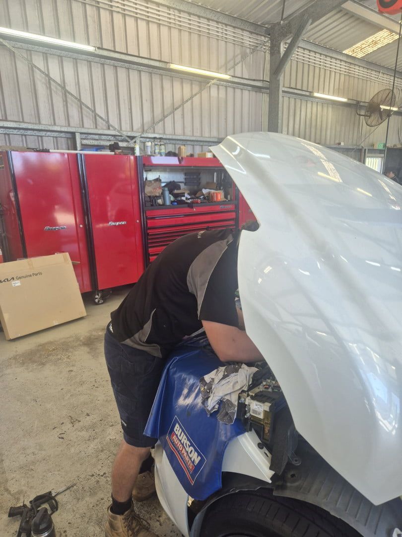 Person Working Under Raised Hood of White Car in a Garage — Emu Park Automotive and Tyre Service in Emu Park, QLD