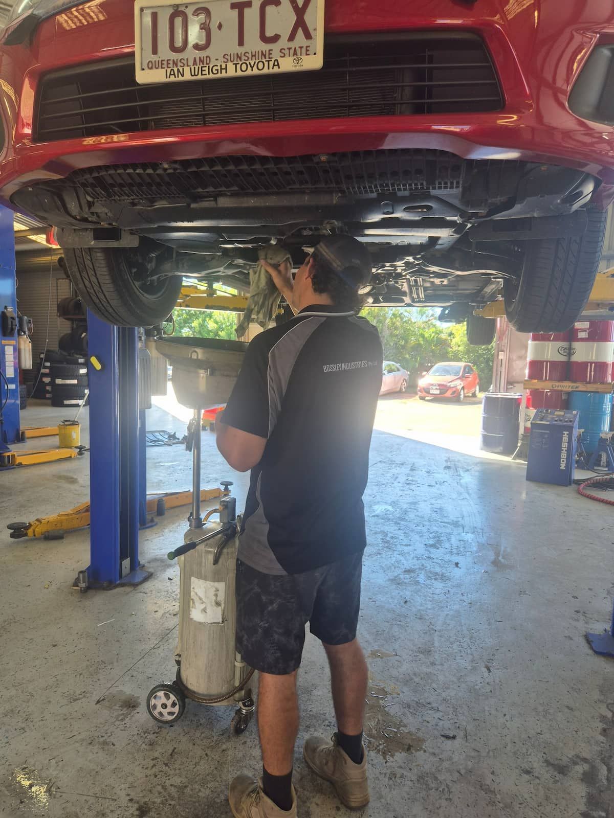 Mechanic working under a red car on a lift in an auto shop — Emu Park Automotive and Tyre Service in Zilzie, QLD