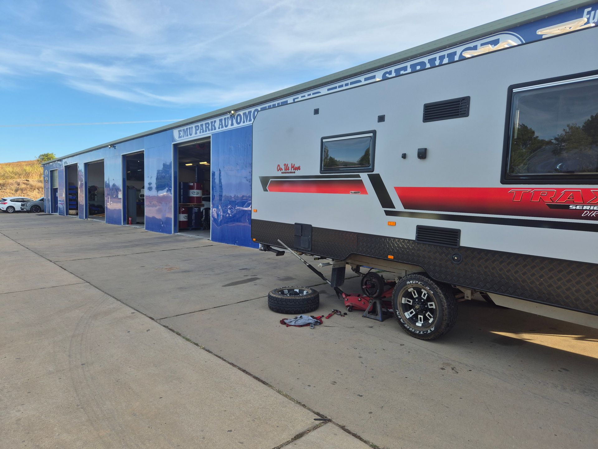 RV in front of blue auto service bays, with a tire and tools on the ground. — Emu Park Automotive and Tyre Service in Keppel Sands, QLD