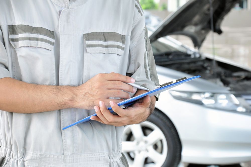 Mechanic Is Holding a Clipboard in Front of A Car with The Hood Open — Emu Park Automotive and Tyre Service in Emu Park, QLD