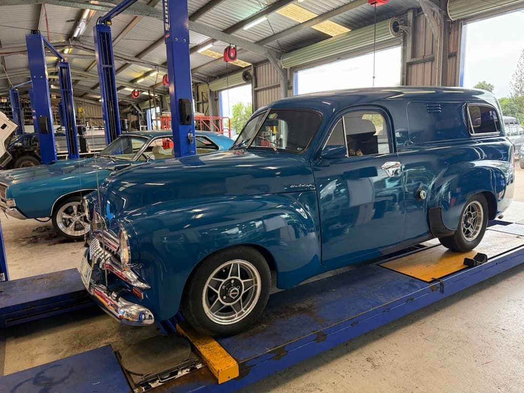 Blue vintage panel van on a lift in a garage, with another classic car in the background.  — Emu Park Automotive and Tyre Service in Emu Park, QLD
