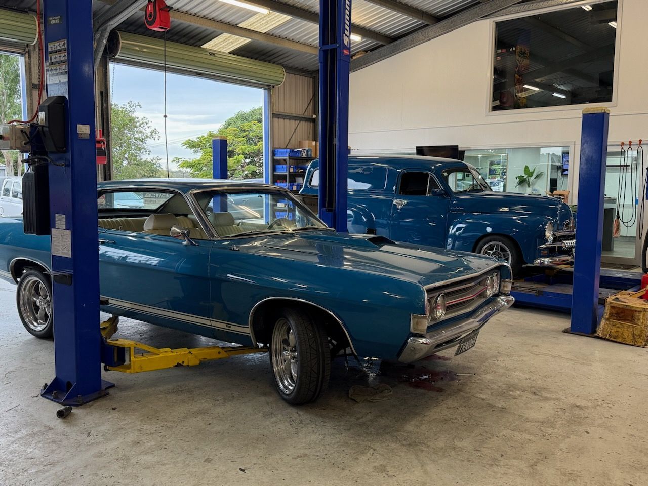 Classic blue car in an auto shop bay, with another blue car on a lift behind it.  — Emu Park Automotive and Tyre Service in Emu Park, QLD