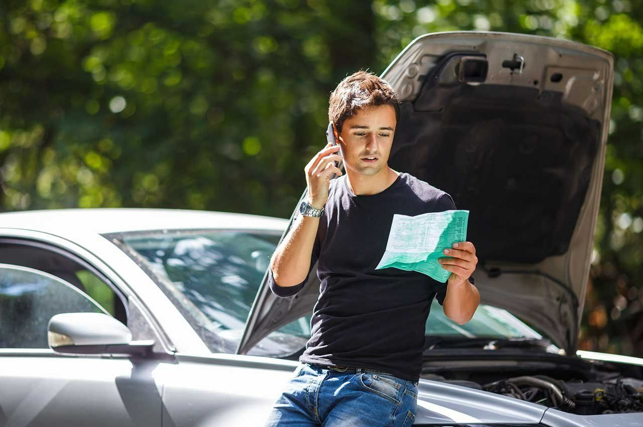 A Man Is Standing Next to A Broken Down Car Talking on A Cell Phone — Emu Park Automotive and Tyre Service in Emu Park, QLD