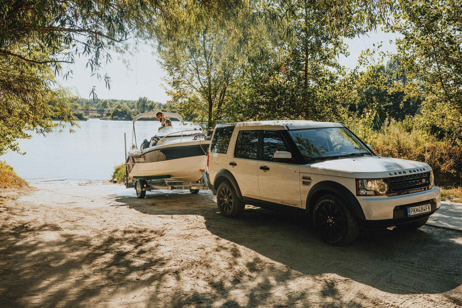 White SUV towing a boat on a dirt road beside a lake under trees — Emu Park Automotive and Tyre Service in Kinka Beach, QLD