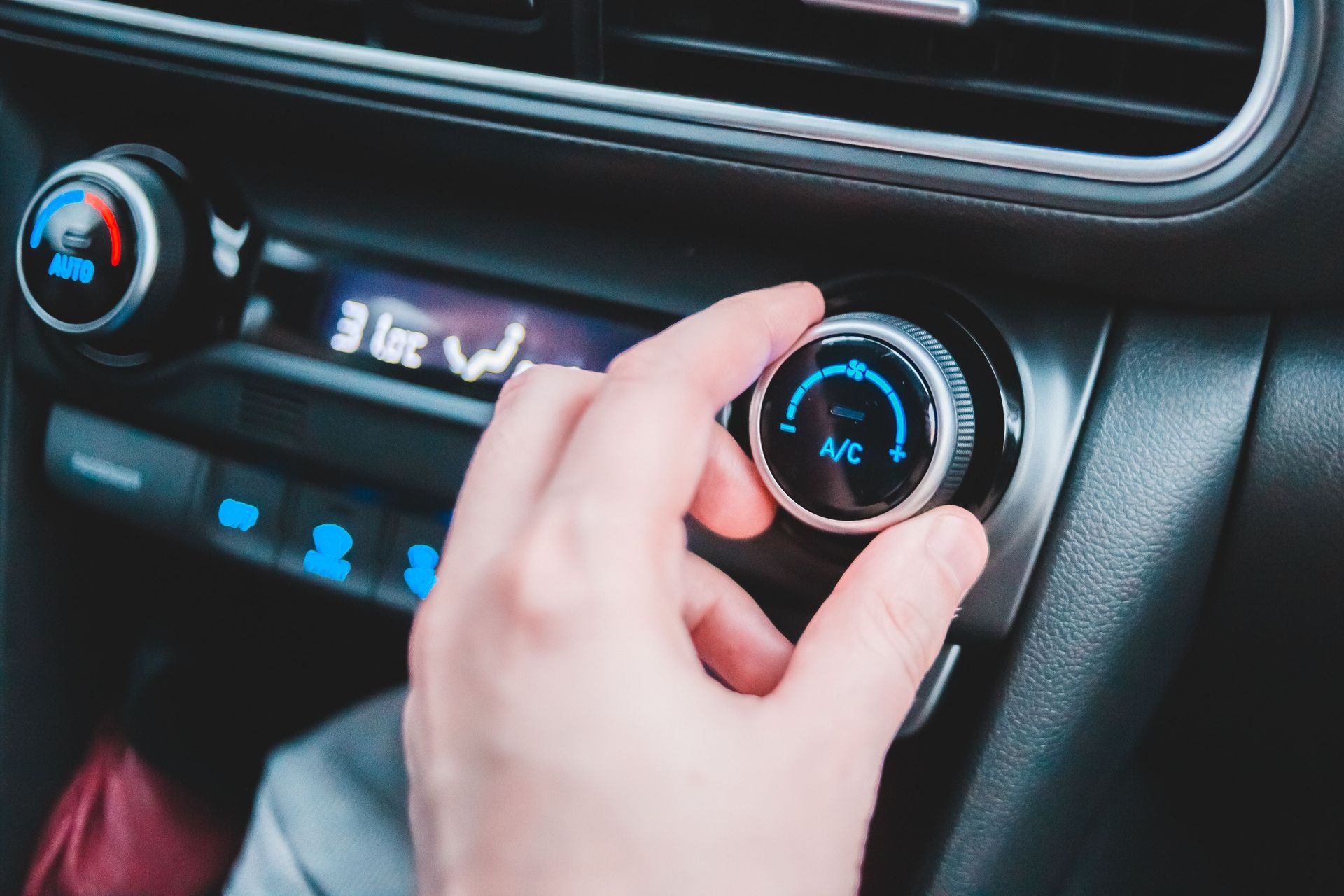 Hand adjusting a car’s climate control knob on a dashboard with blue-lit display and vents  — Emu Park Automotive and Tyre Service in Emu Park, QLD