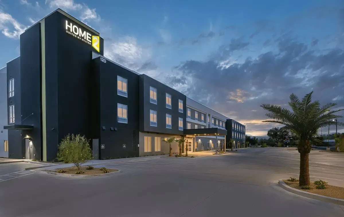 Home2 Suites hotel exterior at dusk, dark gray building with lit windows, palm tree in front.
