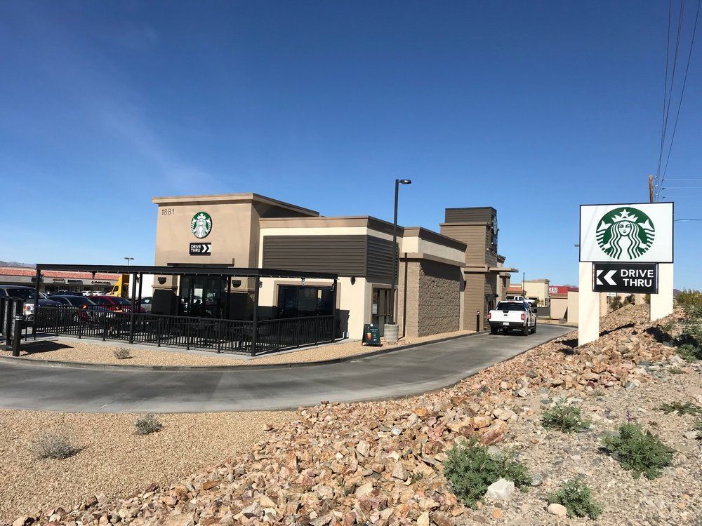 Starbucks store with drive-thru; beige exterior, black awning, sign with logo, drive-thru lane with vehicle, clear blue sky.