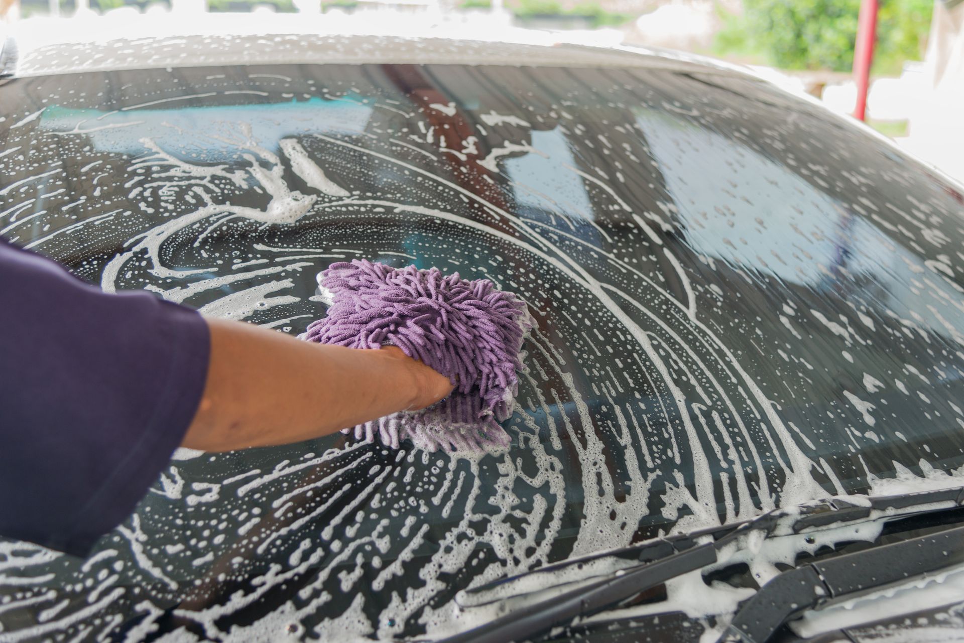 A person is washing a red car with a sponge.