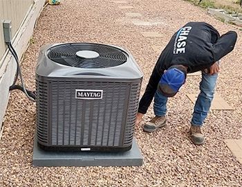 A man is bending over to look at an air conditioner.