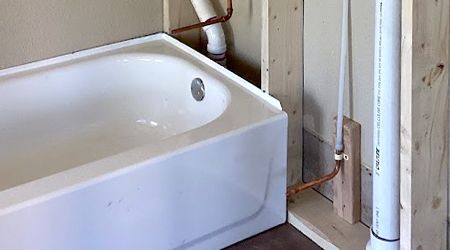 A white bathtub is sitting next to a pipe in a bathroom.