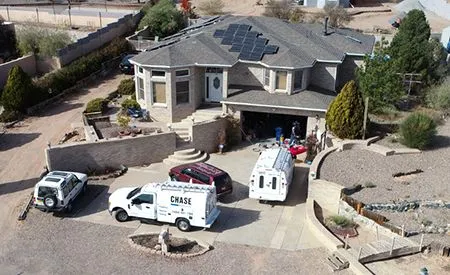 Two utility trucks and a car parked outside a suburban house with workers near the open garage.