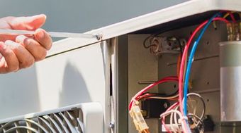 A person is fixing an air conditioner with a screwdriver.