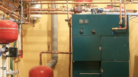 A green boiler is sitting in a room with copper pipes.
