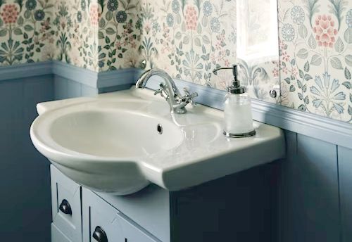 Bathroom sink with floral wallpaper, light blue paneling, and a soap dispenser.