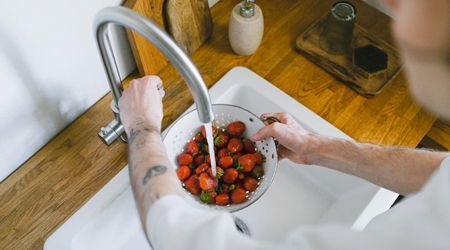 A man is washing strawberries in a bowl in a kitchen sink.