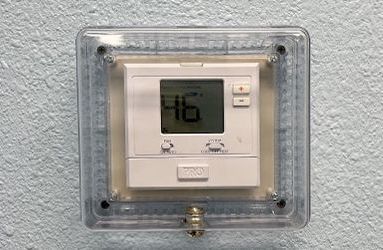 A digital thermostat is mounted on a white wall.