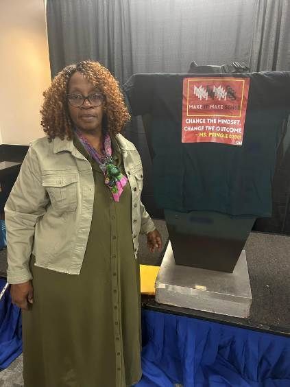 Woman beside a table with a black t-shirt. The shirt has a design of running figures and text.