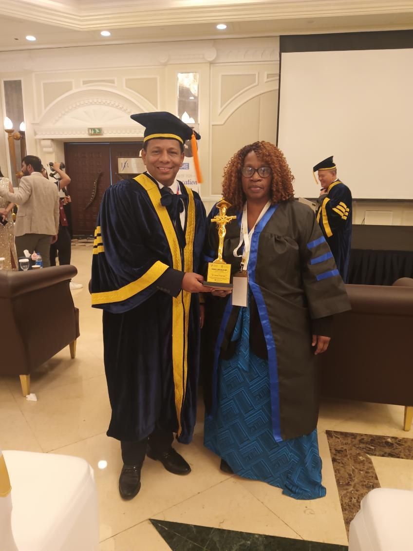 Person in academic robe presenting award to woman in similar attire at an event.