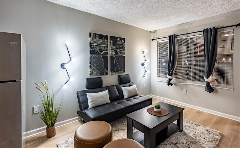 Modern Apartments For Rent In Nashville, TN - Riverwalk 803 - Living Room With Vinyl Plank Flooring, Area Rug, Leather Couch, Coffee Table, Leather Ottoman Stools, And Large Double Window.