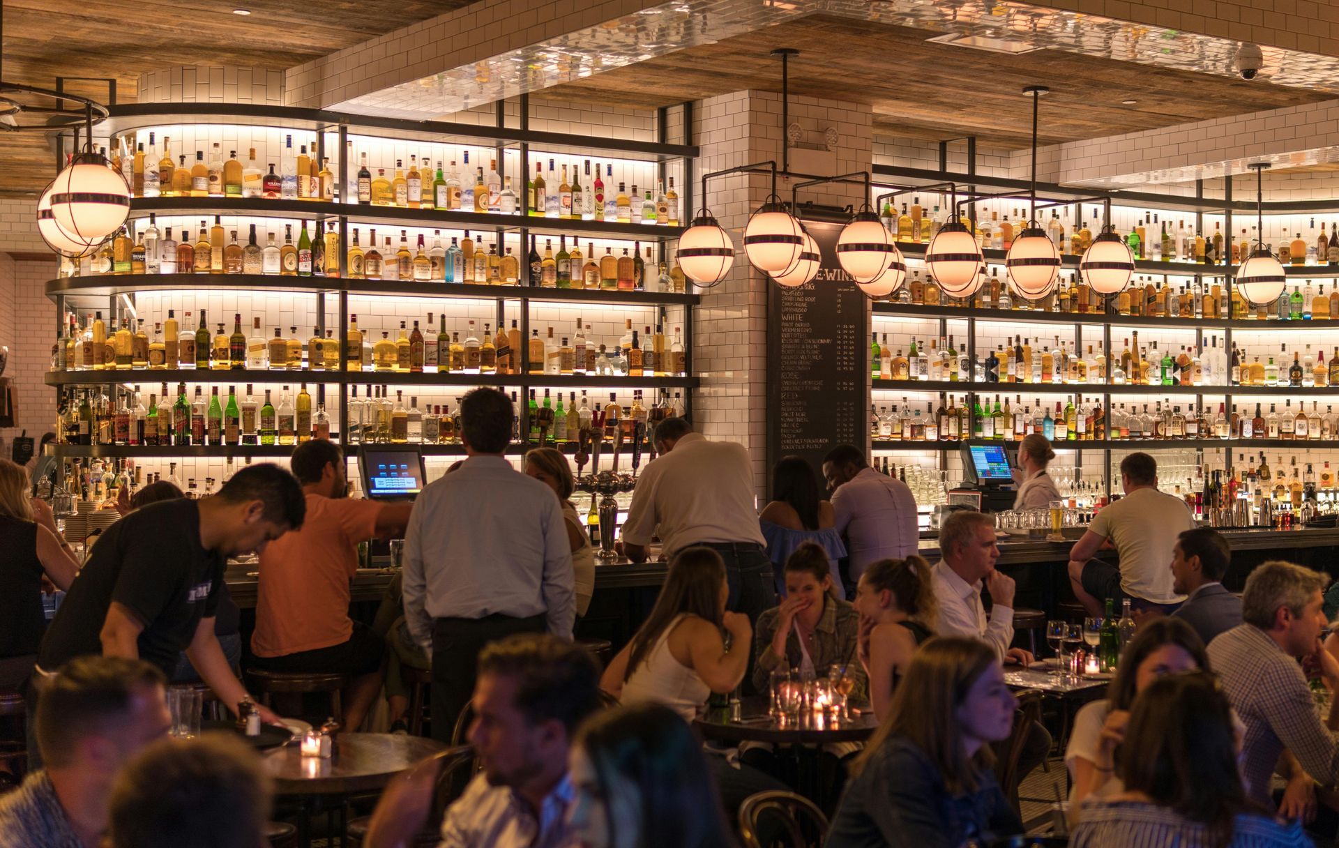 Bar interior with people, liquor shelves, globe lights, and a brick ceiling.