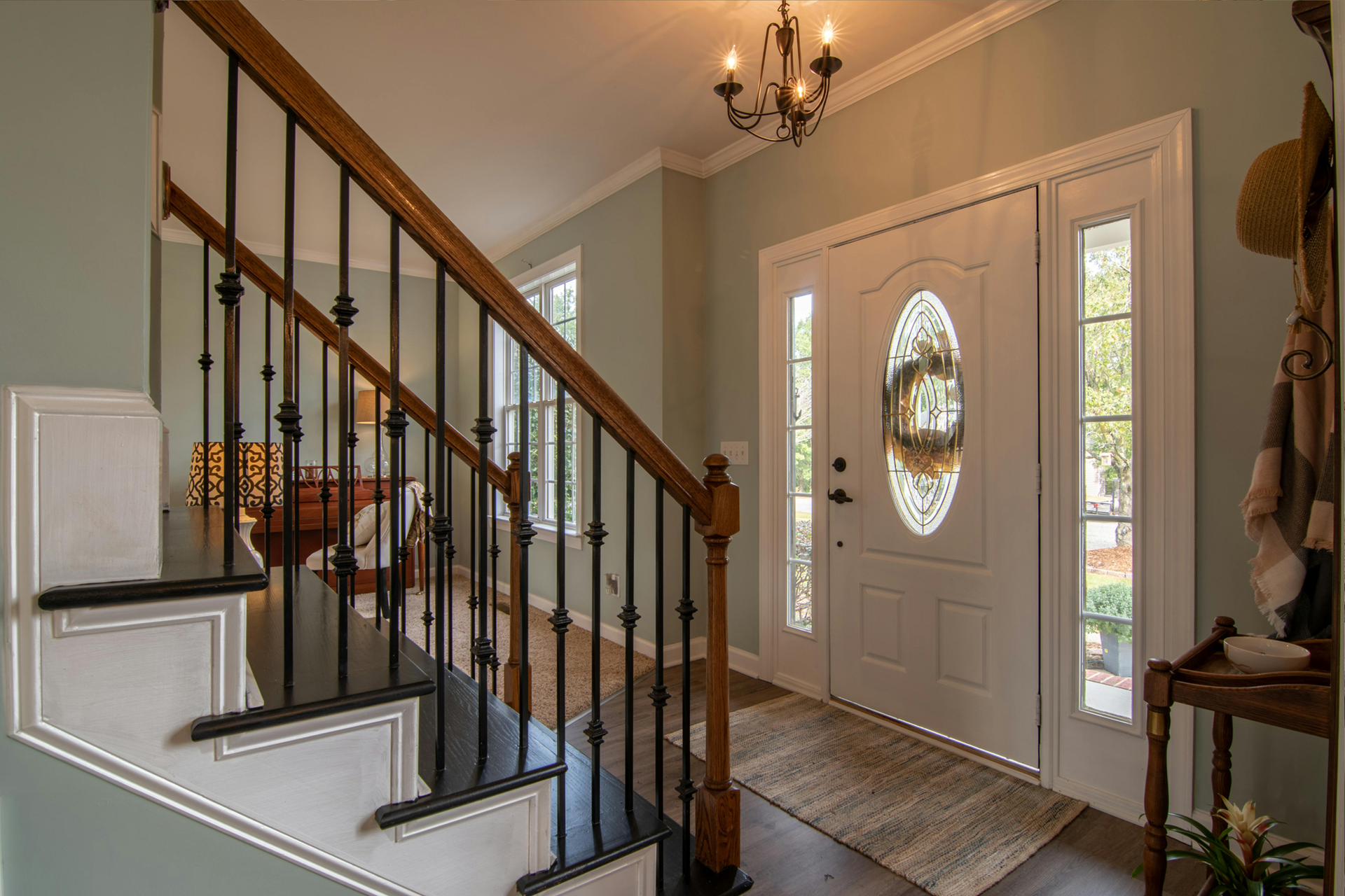 Entryway with stairs and front door, featuring a rug, chandelier, and a decorative table.